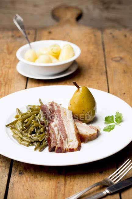 Bacon with beans, a pear and salted potatoes — Stock Photo