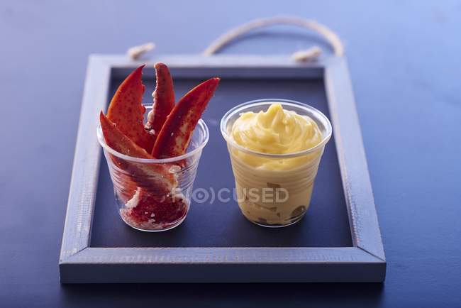 Vista de cerca de las garras de langosta y mayonesa en dos tazas de plástico sobre pizarra negra - foto de stock