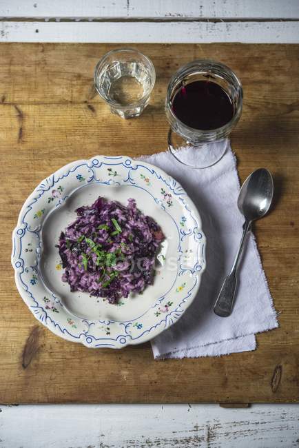 Red cabbage risotto with basil on plate over wooden surface with napkin and spoon — Stock Photo