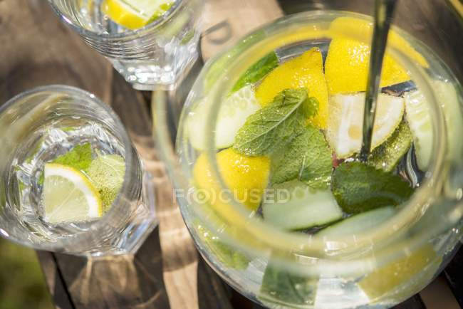 Lemon water with cucumber and mint on a wooden crate in the garden — Stock Photo