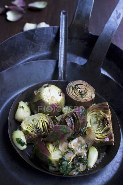Alcachofas con hierbas y ajo en una sartén de hierro forjado a mano - foto de stock