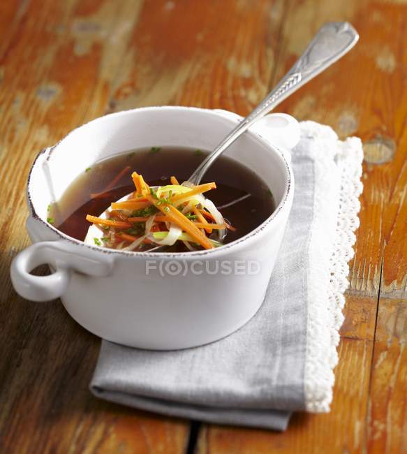 Meat broth with julienned vegetables in white dish with spoon on wooden surface — Stock Photo