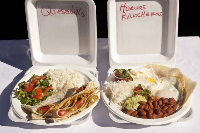 Мексиканская уличная еда: кесадильи и хуэвос ранчерос на пластиковых тарелках — стоковое фото