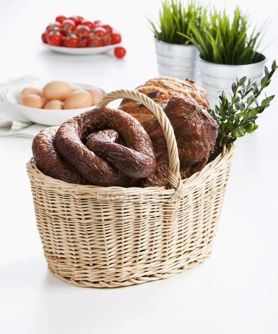 Various sausages and ham in an Easter basket over white background — Stock Photo