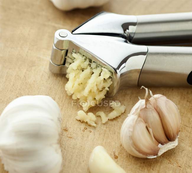 Garlic crusher and garlic bulbs — Stock Photo