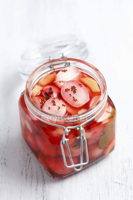 Pickled radishes in preserving jar on white wooden surface — Stock Photo