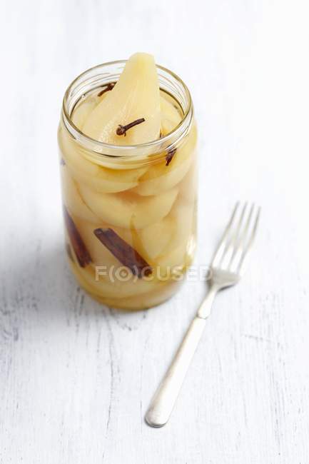 Pears pickled in vinegar in jar over white wooden surface with fork — Stock Photo