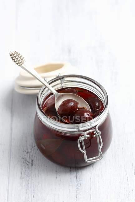 Closeup view of preserved plums with spoon in glass jar — Stock Photo