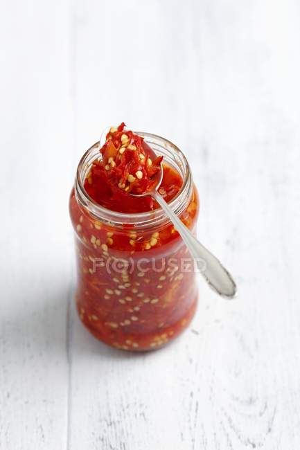 Pickled chillies em frasco com colher sobre superfície de madeira branca — Fotografia de Stock