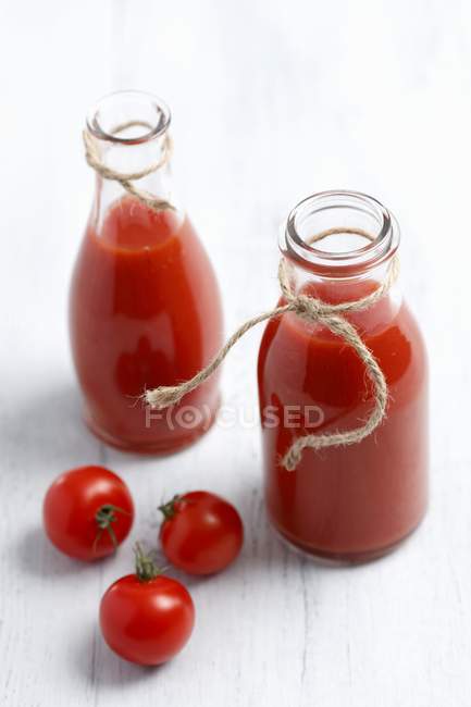 Homemade tomato puree in bottles on white wooden surface — Stock Photo