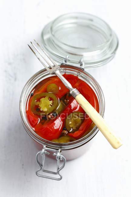 Pickled pepper and jalapeno in glass jar with fork over white surface — Stock Photo