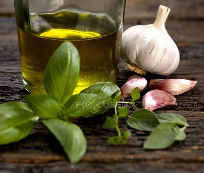 Garlic , sage thyme, basil and olive oil ingredients for dressing on wooden surface — Stock Photo