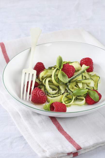 Zucchine con lamponi e pesto su piatto bianco con forchetta sopra asciugamano — Foto stock