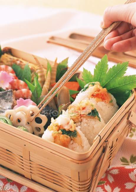 Déjeuner avec des rouleaux et des légumes dans une caisse en bois et la main avec des bâtons en bois sur — Photo de stock