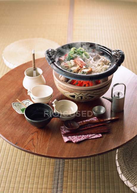 Elevated view of steaming vegetable dish on embers and crockery on wooden Asian table — Stock Photo