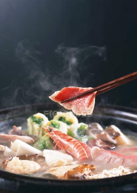 Vista de cerca del guiso japonés con la pieza de pescado en palillos - foto de stock