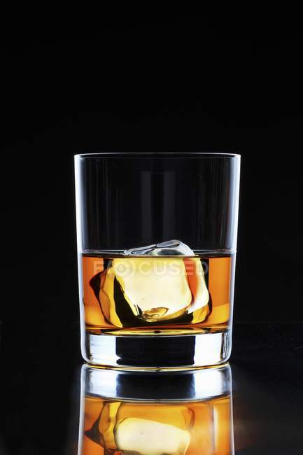 Glass of whiskey with an ice cube — Stock Photo
