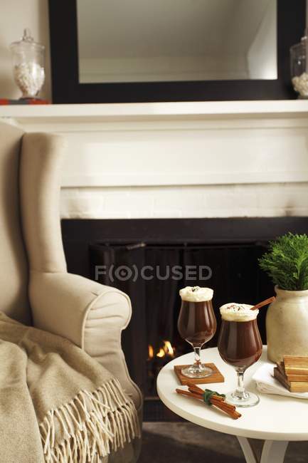 Irish coffee in two glasses on table near fireplace — Stock Photo