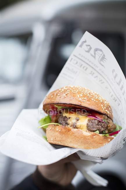 Mão segurando hambúrguer em papel — Fotografia de Stock
