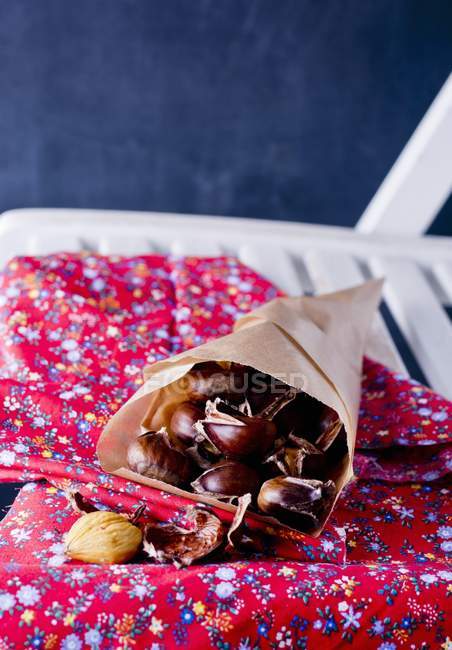 Nahaufnahme von Kastanien in einer Papiertüte mit blumig gemustertem Tuch auf Stuhl — Stockfoto