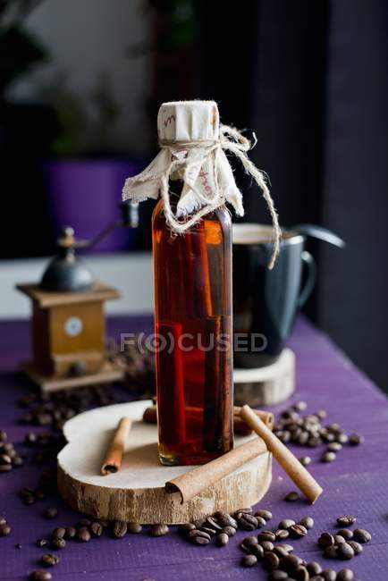 Крупный план сиропа с корицей в бутылке с палочками корицы и кофейными зёрнами — стоковое фото