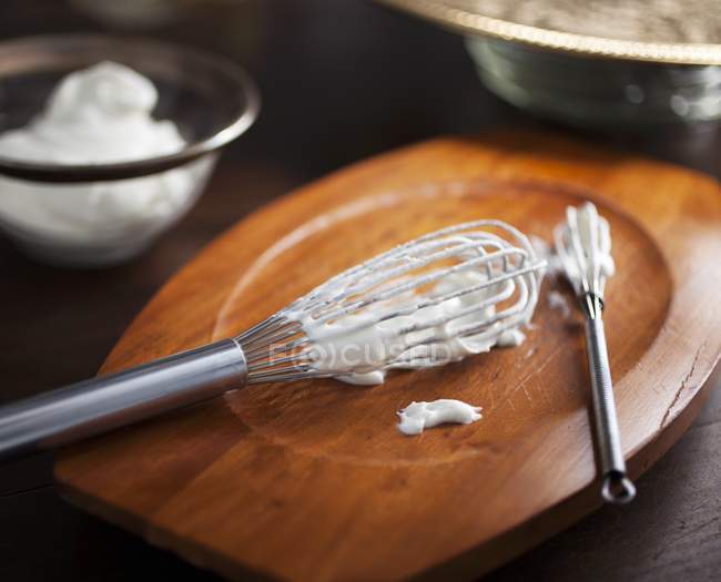 Closeup view of two whisks with freshly whipped cream on a wooden board — Stock Photo