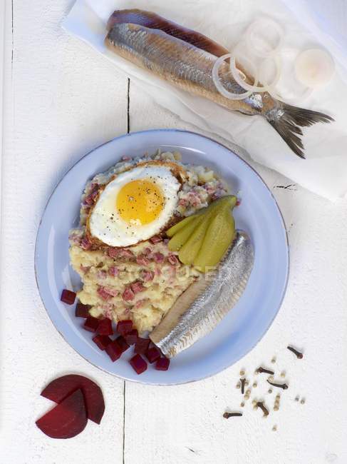 Labskaus - traditional dish featuring herring, egg and gherkins on blue plate — Stock Photo
