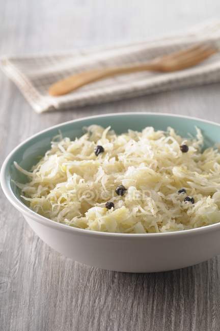 Sauerkraut with juniper berries on white plate over wooden surface — Stock Photo