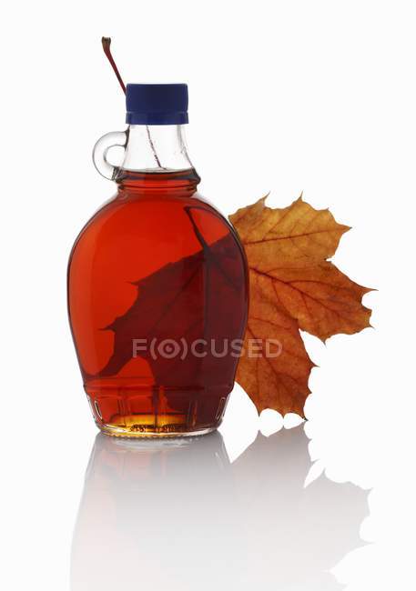 Вид крупным планом на кленовый сироп в стеклянной бутылке и кленовый лист — стоковое фото