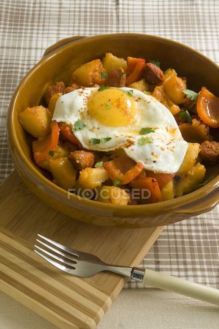 Картофель с чоризо, перец и жареное яйцо в коричневом блюде над деревянным столом — стоковое фото