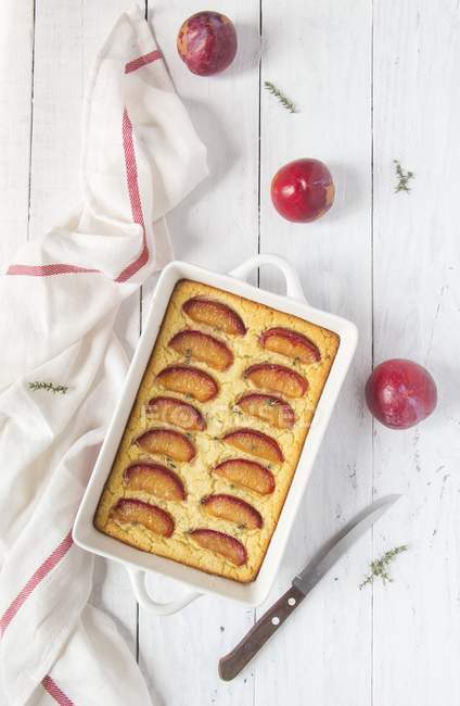 Plum clafoutis in white dish with towel over wooden surface — Stock Photo