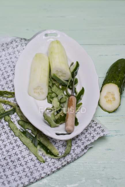 A peeled cucumber on a white porcelain plate with a peeler and peel on white plate — Stock Photo