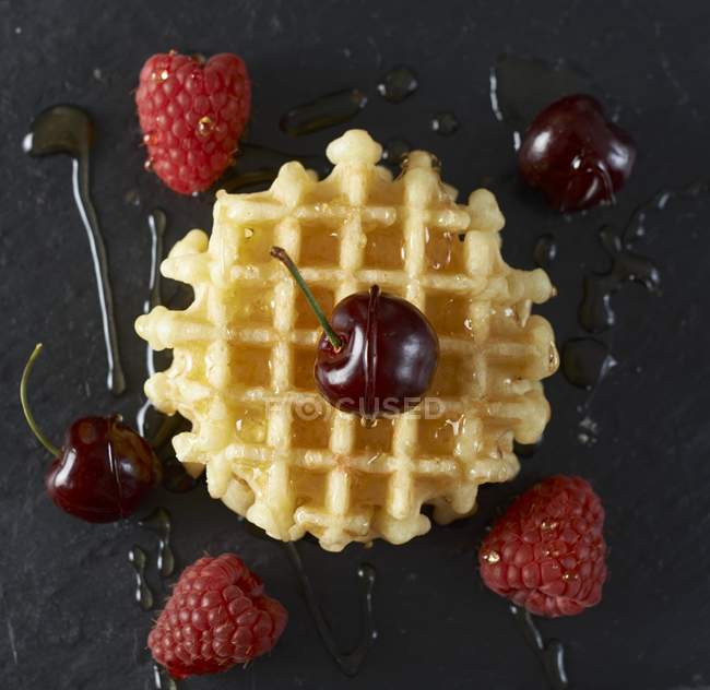 Closeup top view of Belgian waffle with cherries, raspberries and maple syrup — Stock Photo