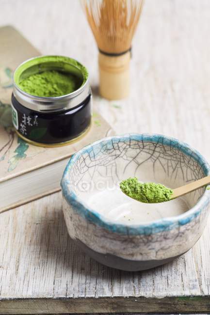 Elevated view of Matcha tea powder in spoon over bowl and in tin — Stock Photo