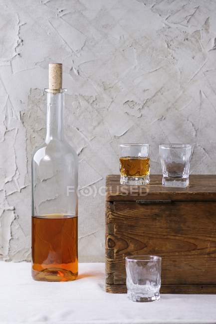 Vista de perto de rum e três copos no peito de madeira na frente da parede rebocada — Fotografia de Stock