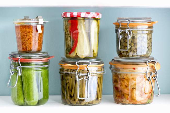 Pickled vegetables in preserving jars against blue background — Stock Photo