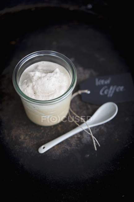 Elevated view of iced coffee in a jar with a porcelain spoon on a dark surface — Stock Photo