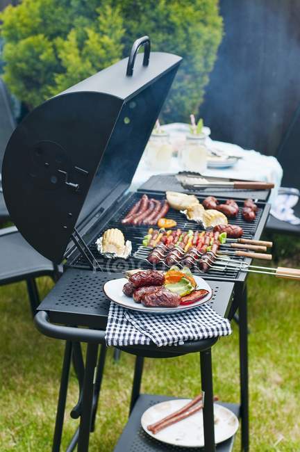 Enchidos, espetos e legumes em um churrasco de carvão ao ar livre durante o dia — Fotografia de Stock
