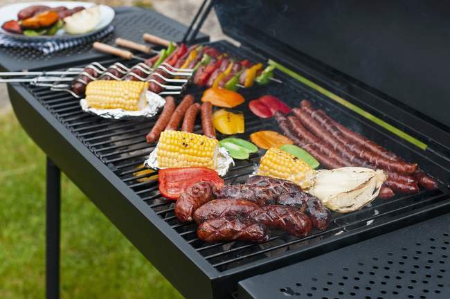 Elevated view of sausages, skewers and vegetables on a charcoal barbecue — Stock Photo