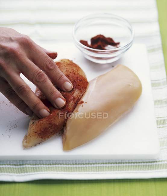 Vista close-up de mão esfregando pedaços de peito de frango com especiarias — Fotografia de Stock