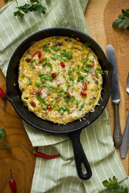 An omelette with parsley and chilli rings on black frying pan over towel — Stock Photo