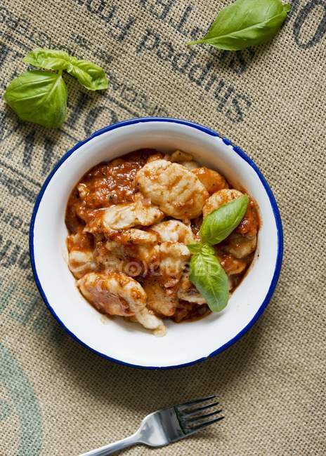 Gnocchi with tomato sauce and basil on white plate over textile surface with fork — Stock Photo