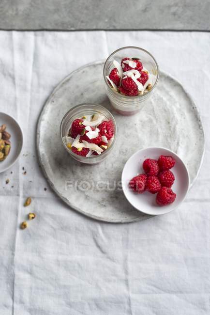 Primer plano vista superior del yogur con frambuesas frescas, pistachos y copos de coco - foto de stock