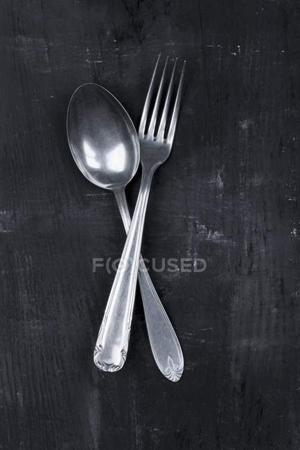 Vista de cerca de una cuchara vieja y tenedor cruzado sobre una superficie negra - foto de stock