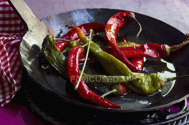 Chillis vermelhos e verdes fritos em azeite em uma panela preta de ferro fundido — Fotografia de Stock