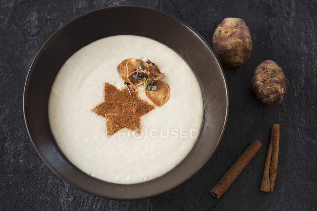 Cream of Jerusalem artichoke soup with cinnamon on black plate — Stock Photo