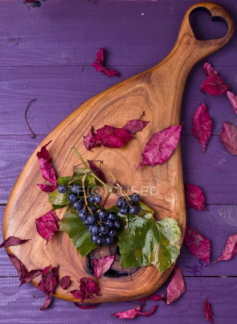 Grapes and autumnal leaves on a wooden board — Stock Photo