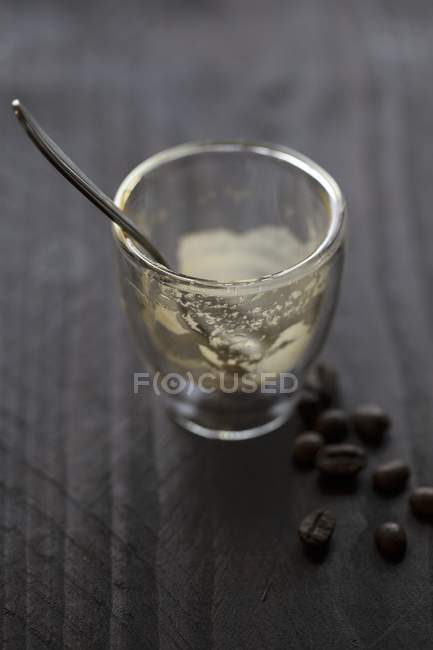 Vista de perto de vidro Espresso com restos, colher e grãos de café na superfície de madeira — Fotografia de Stock