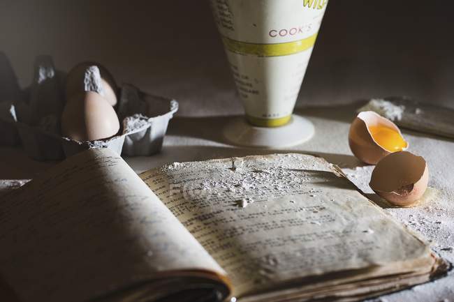 Nahaufnahme eines geöffneten alten Rezeptbuchs, Eier und Mehl — Stockfoto