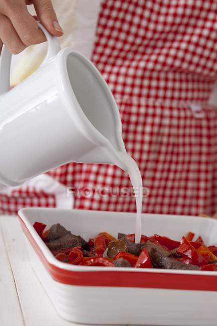 Cropped view of woman pouring creamy sauce over beef with peppers — Stock Photo